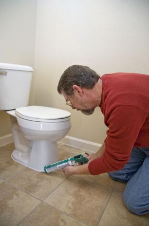 Plumber in Monterey, CA caulks a toilet